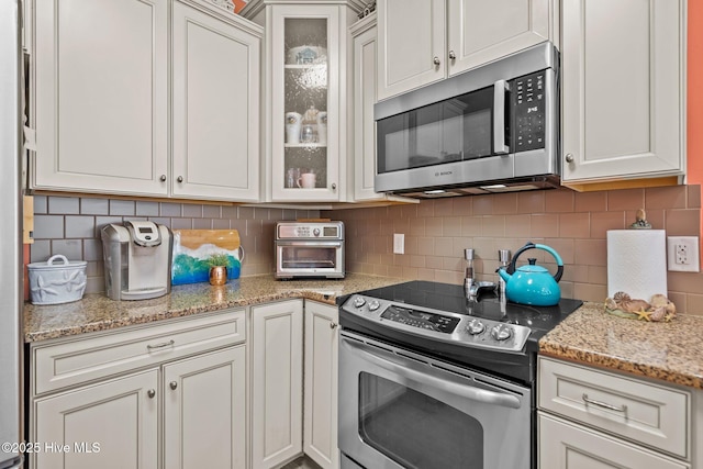 kitchen with light stone counters, appliances with stainless steel finishes, glass insert cabinets, and decorative backsplash