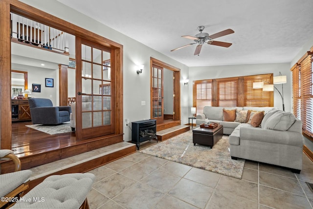 living room featuring a wood stove, tile patterned floors, a ceiling fan, and a healthy amount of sunlight