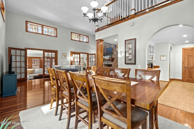 dining room featuring arched walkways, a high ceiling, a textured ceiling, wood finished floors, and a chandelier