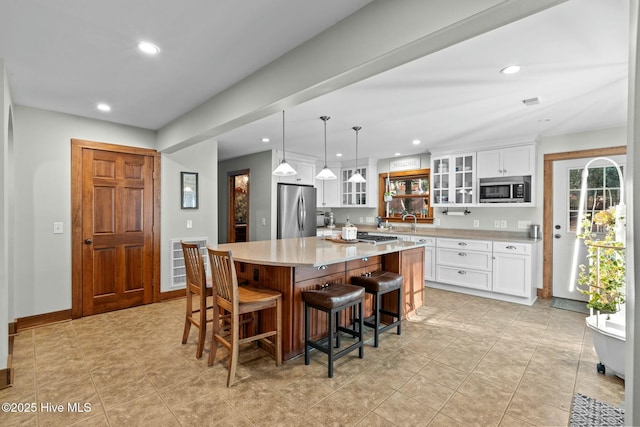 kitchen featuring glass insert cabinets, a kitchen island, white cabinets, appliances with stainless steel finishes, and decorative light fixtures