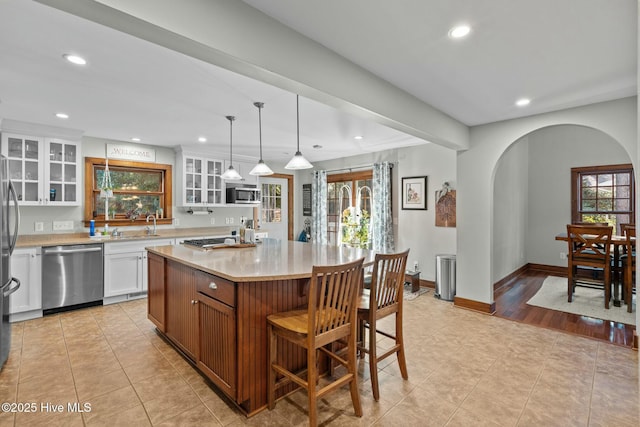 kitchen with stainless steel appliances, glass insert cabinets, a kitchen island with sink, and white cabinets