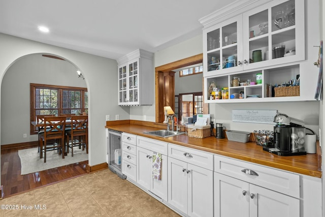 kitchen featuring wine cooler, open shelves, glass insert cabinets, white cabinetry, and a sink