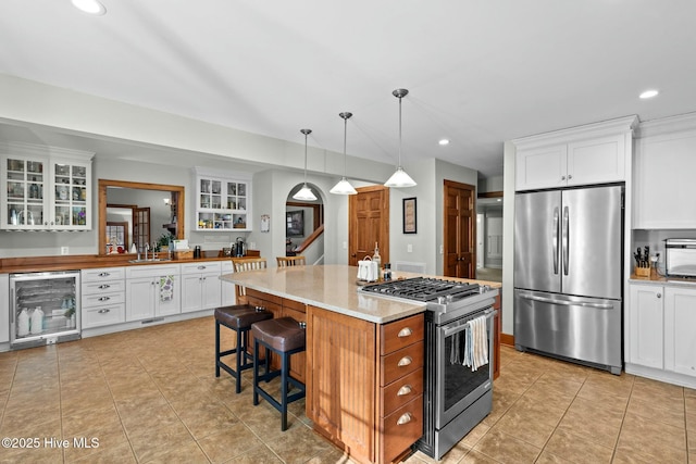 kitchen with beverage cooler, stainless steel appliances, white cabinetry, a center island, and glass insert cabinets