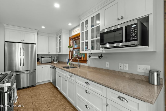 kitchen featuring appliances with stainless steel finishes, glass insert cabinets, white cabinets, a sink, and light stone countertops