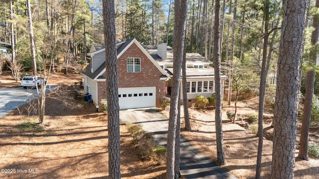 view of front of house featuring dirt driveway, a chimney, an attached garage, central air condition unit, and brick siding