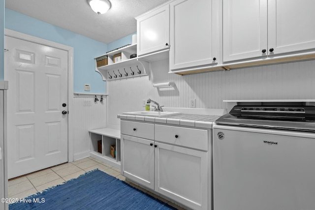 laundry area with light tile patterned floors, a wainscoted wall, a sink, and cabinet space