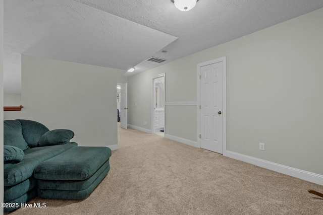 sitting room with light colored carpet, visible vents, a textured ceiling, and baseboards