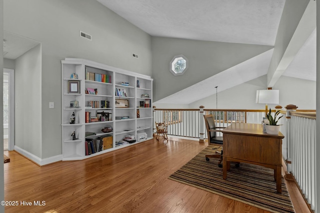 living area with high vaulted ceiling, wood finished floors, an upstairs landing, visible vents, and baseboards