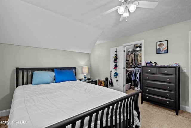 bedroom featuring a walk in closet, a closet, light colored carpet, vaulted ceiling, and baseboards