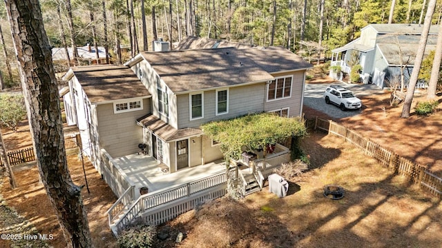 view of front facade featuring roof with shingles, driveway, a deck, and fence