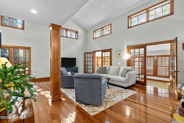 living room with ornate columns, high vaulted ceiling, wood finished floors, and french doors