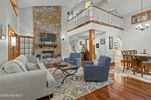 living room with a chandelier, arched walkways, a high ceiling, a fireplace, and wood finished floors