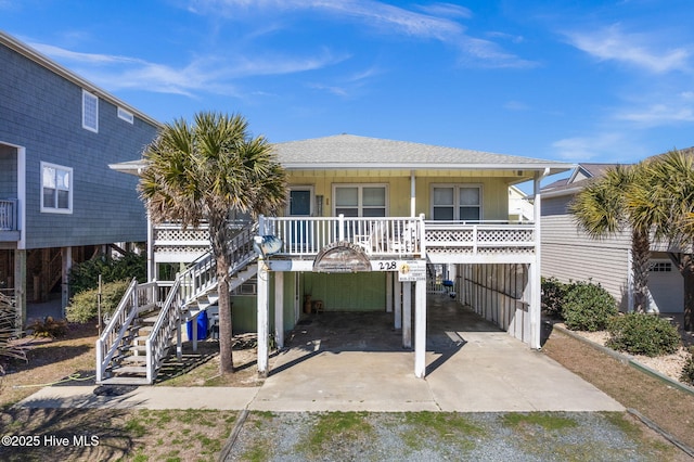 beach home with driveway, covered porch, stairway, and roof with shingles