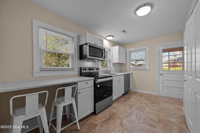 kitchen with sink, backsplash, light stone counters, appliances with stainless steel finishes, and white cabinets