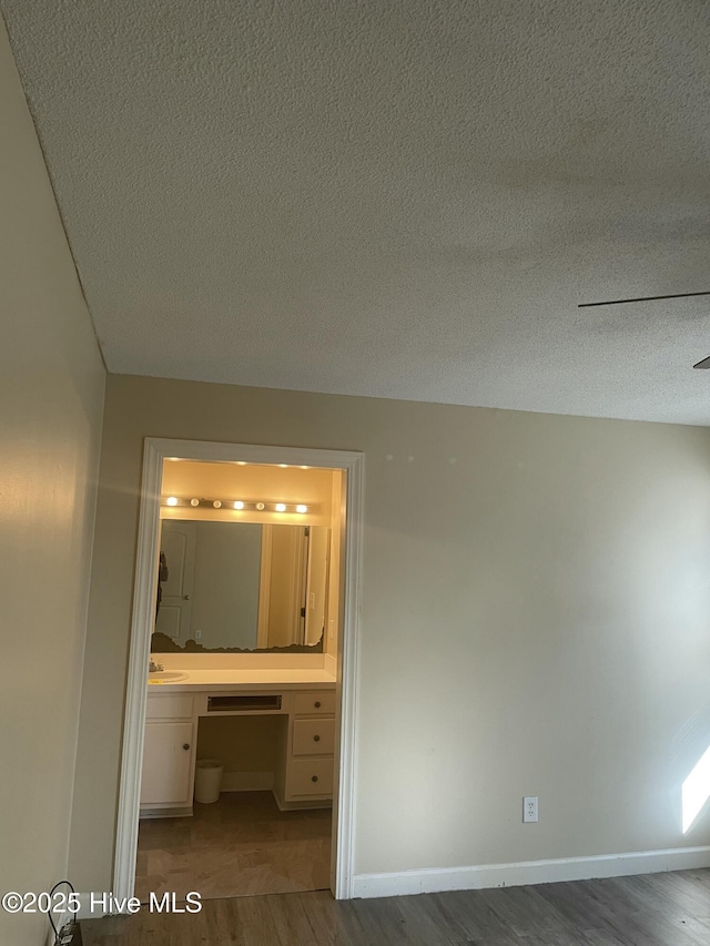 unfurnished bedroom featuring built in desk, ensuite bath, wood-type flooring, and a textured ceiling