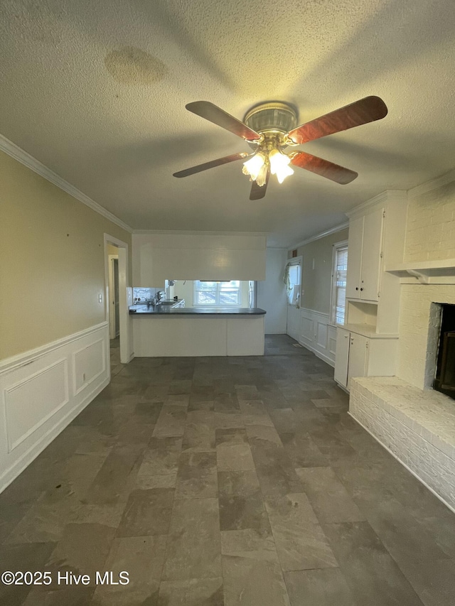 unfurnished living room with a brick fireplace, a healthy amount of sunlight, a textured ceiling, and ornamental molding