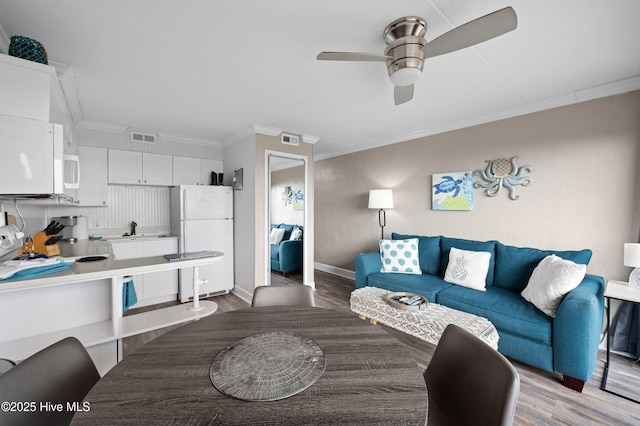 living area with visible vents, baseboards, ceiling fan, ornamental molding, and light wood-style floors