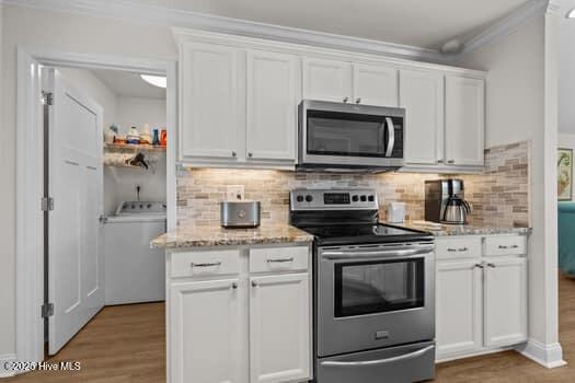 2011 Fisher St, Morehead City, NC 28557 - kitchen featuring appliances with stainless steel finishes, washer / clothes dryer, white cabinetry, light wood-type flooring, and crown molding
