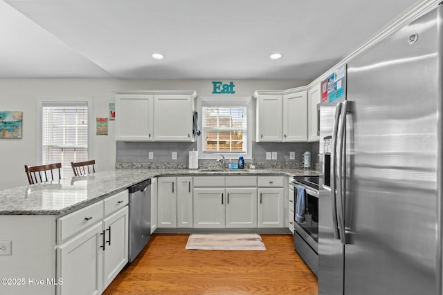 kitchen with stainless steel appliances, tasteful backsplash, white cabinetry, a sink, and a peninsula