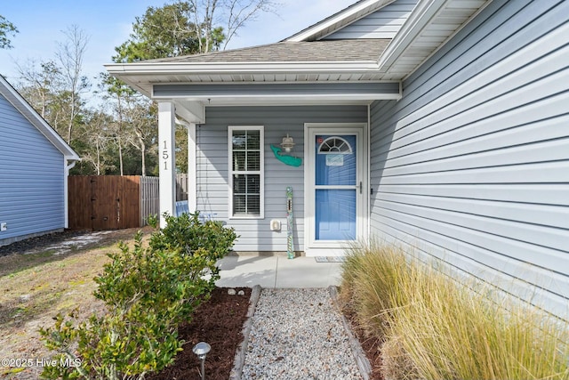 entrance to property featuring a shingled roof, fence, and a porch