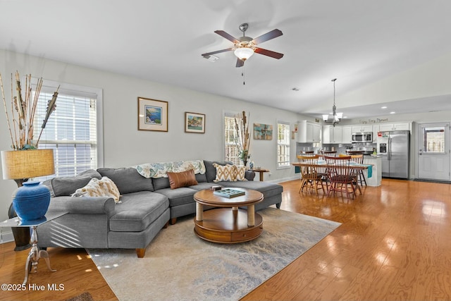 living area featuring lofted ceiling, a healthy amount of sunlight, light wood finished floors, and ceiling fan with notable chandelier