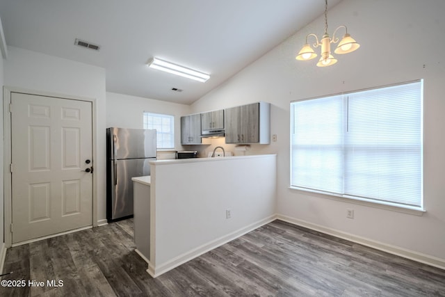 kitchen with light countertops, hanging light fixtures, visible vents, freestanding refrigerator, and a peninsula