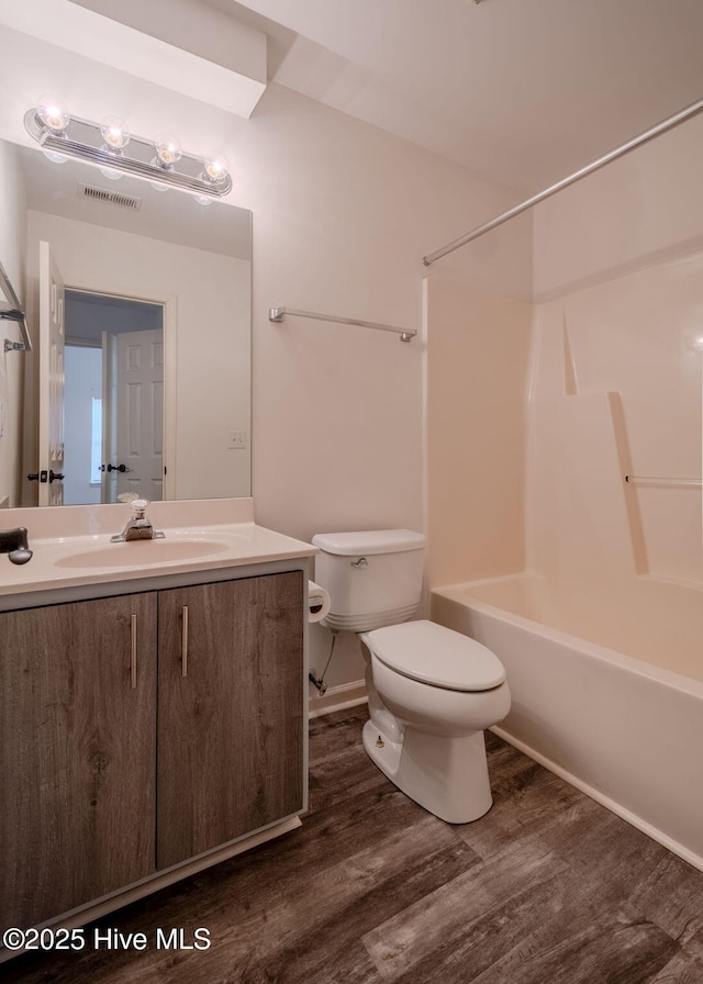 bathroom with visible vents, toilet, vanity, wood finished floors, and  shower combination