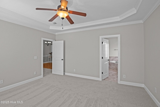 unfurnished bedroom featuring a tray ceiling, ceiling fan with notable chandelier, connected bathroom, crown molding, and light colored carpet