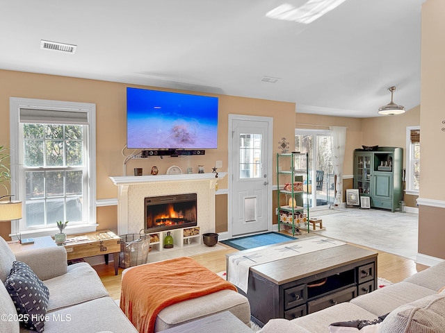 living area with a fireplace with flush hearth, light wood-type flooring, visible vents, and baseboards