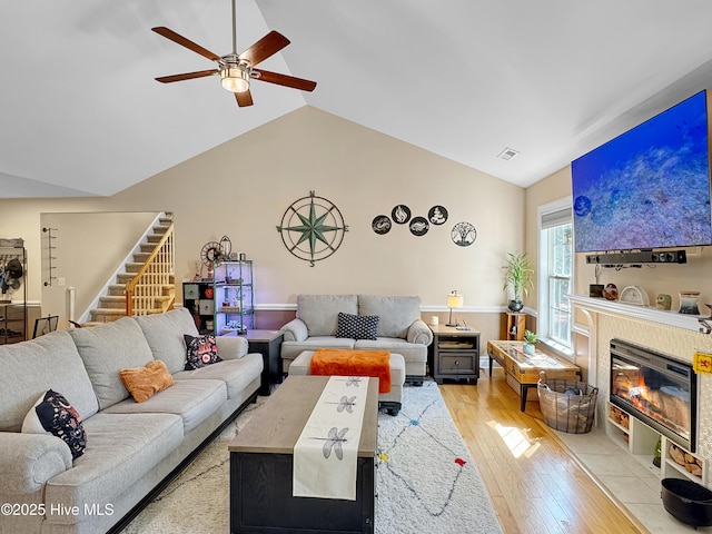 living room featuring lofted ceiling, a fireplace with flush hearth, ceiling fan, wood finished floors, and stairs