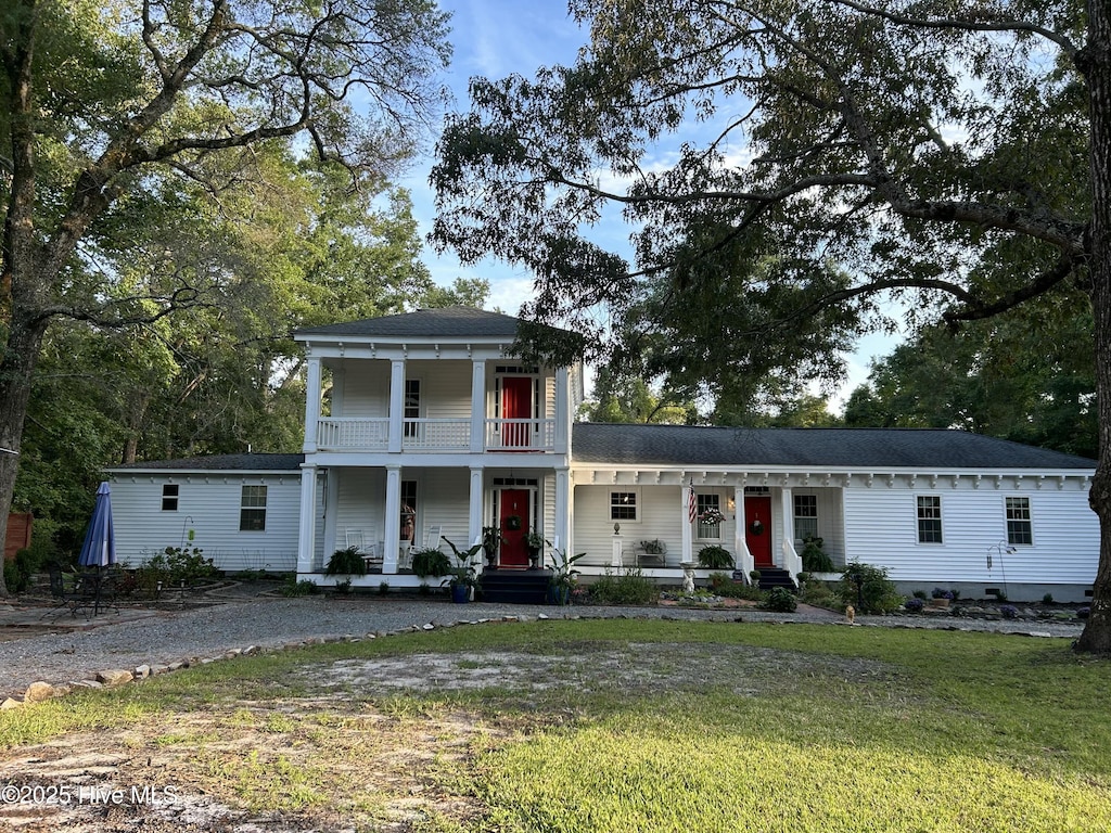 greek revival house with covered porch, a balcony, a front lawn, a shingled roof, and driveway