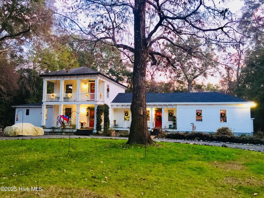 greek revival house featuring a balcony, covered porch, and a front yard