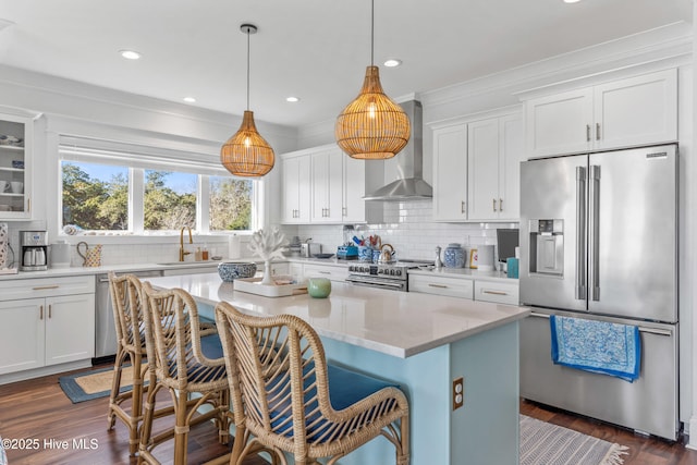 kitchen with appliances with stainless steel finishes, wall chimney range hood, white cabinetry, glass insert cabinets, and a kitchen island