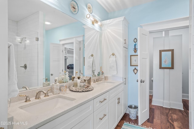 bathroom featuring double vanity, wood finished floors, a sink, and a stall shower