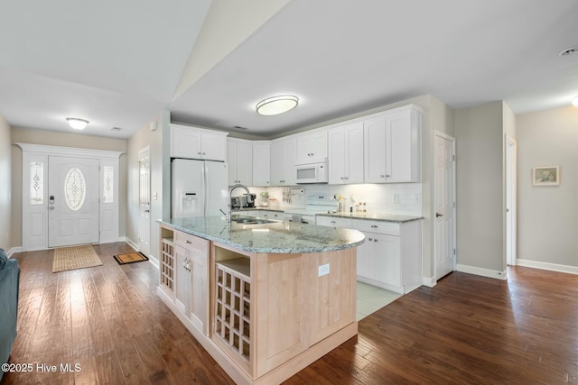 kitchen featuring white appliances, light stone countertops, dark wood-style flooring, a sink, and decorative backsplash