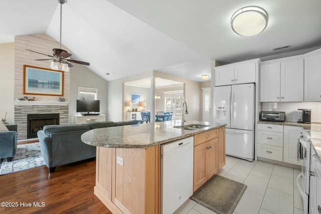 kitchen with visible vents, light stone countertops, lofted ceiling, white appliances, and a sink