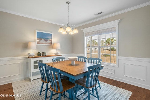 dining room with crown molding, wood finished floors, visible vents, and wainscoting