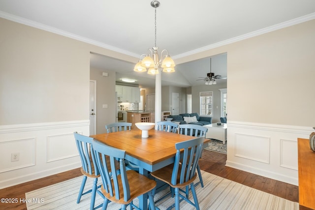 dining room featuring wainscoting, wood finished floors, crown molding, and ceiling fan with notable chandelier