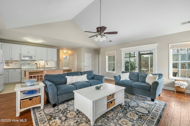 living room featuring hardwood / wood-style floors, a ceiling fan, baseboards, visible vents, and high vaulted ceiling