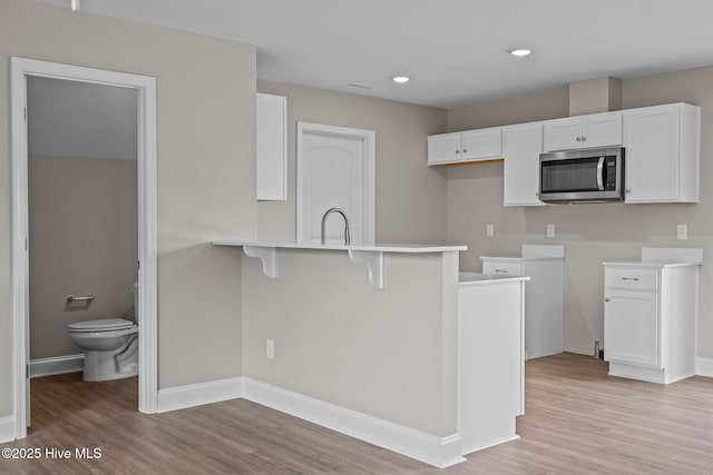 kitchen featuring a peninsula, a kitchen bar, stainless steel microwave, white cabinets, and light wood-style flooring