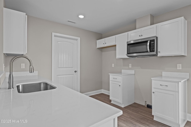 kitchen featuring visible vents, a sink, stainless steel microwave, and white cabinets