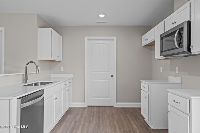 kitchen featuring appliances with stainless steel finishes, a sink, baseboards, wood finished floors, and visible vents