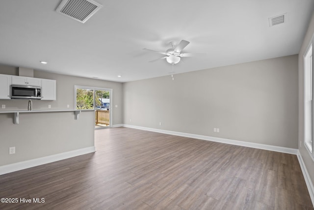unfurnished living room featuring visible vents, baseboards, ceiling fan, and wood finished floors