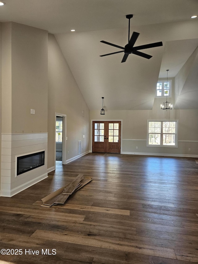 unfurnished living room featuring high vaulted ceiling, ceiling fan with notable chandelier, dark wood-style flooring, french doors, and a glass covered fireplace