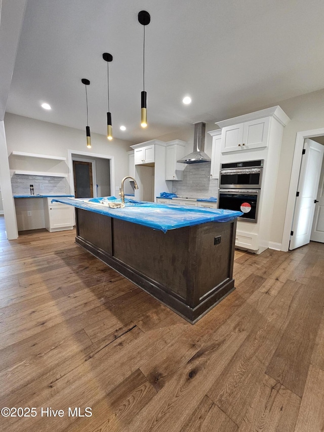 kitchen featuring backsplash, wall chimney exhaust hood, white cabinets, and wood finished floors