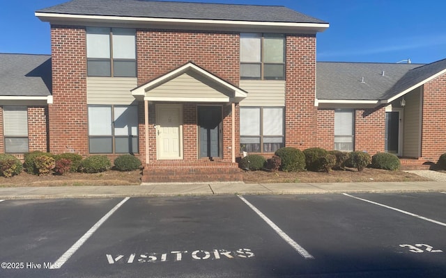 view of front facade with uncovered parking, brick siding, and a shingled roof