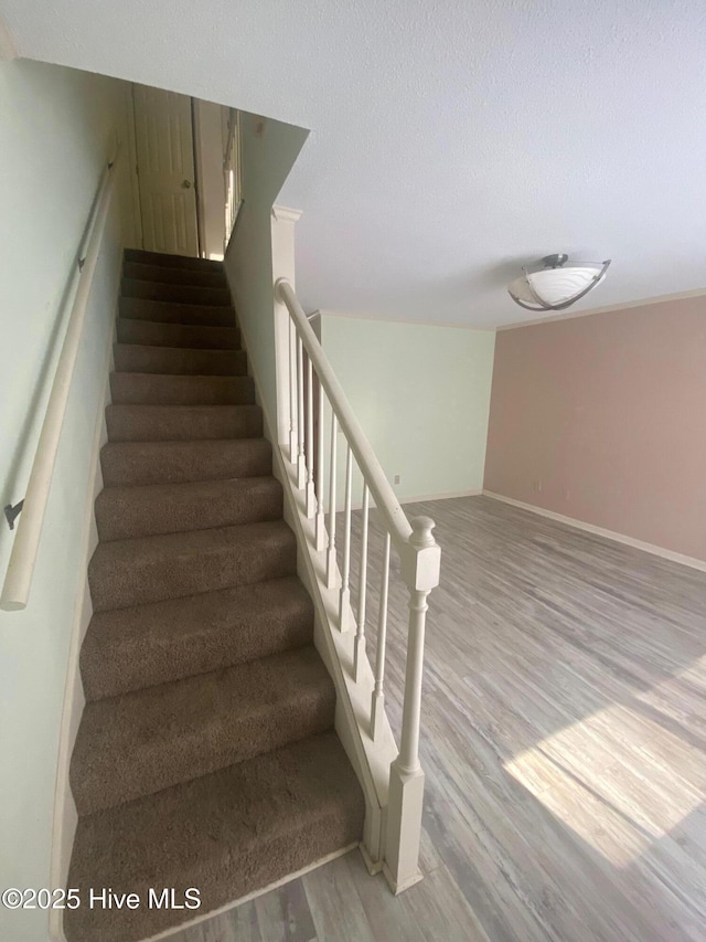 stairs with a textured ceiling, wood finished floors, and baseboards