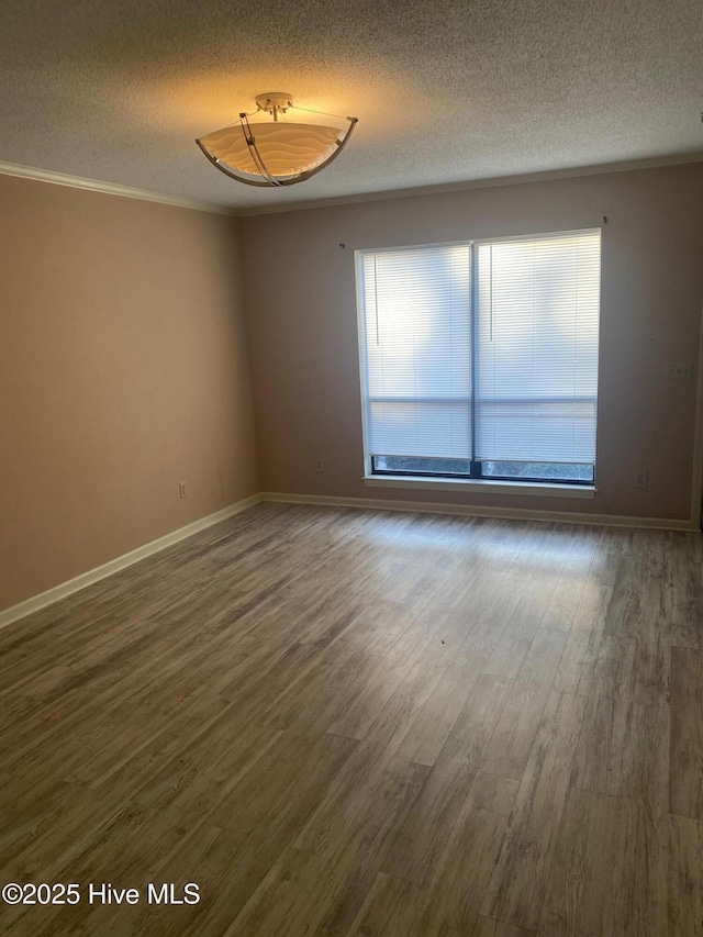 spare room featuring ornamental molding, dark wood-style flooring, a textured ceiling, and baseboards