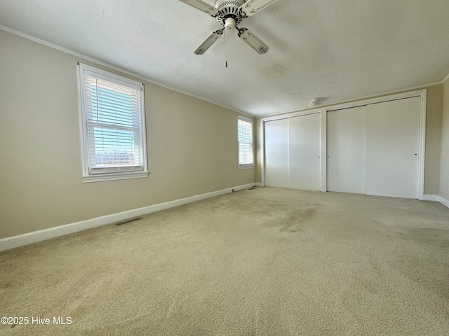 unfurnished bedroom with a textured ceiling, carpet flooring, a ceiling fan, multiple closets, and crown molding