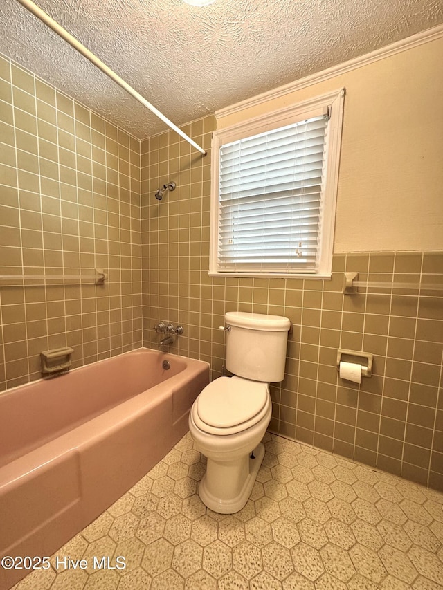 full bath with toilet, a textured ceiling, shower / washtub combination, and tile walls